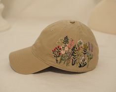 a baseball cap with embroidered flowers on it sitting on a white bedding sheet,