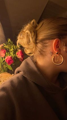 a woman with her hair in a bun wearing large gold hoop earrings and pink roses