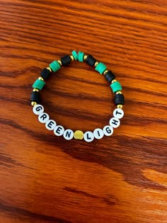 the greenlight bracelet on a wooden table with beads and black, white and gold beads