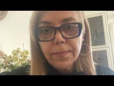 a woman with glasses is taking a selfie in front of a flower pot and window