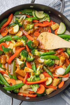 a skillet filled with stir fry vegetables on top of a striped table cloth next to a wooden spoon