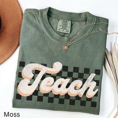 a green t - shirt with the word teach printed on it next to a hat