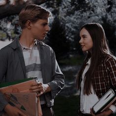 a man and woman standing next to each other in front of a tree holding folders