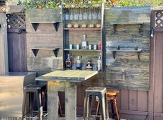 an outdoor bar with two stools next to it and bottles on the back wall