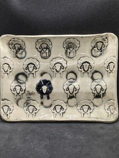 a ceramic tray with sheep on it sitting on a black cloth covered tablecloth in front of a gray background