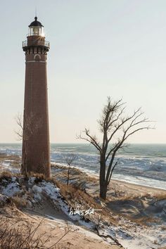 a light house sitting on top of a snow covered hill next to the ocean and trees