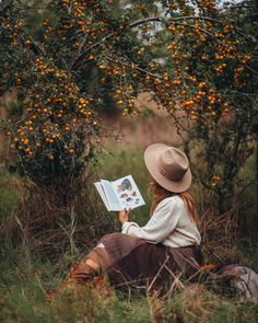 a woman sitting in the grass reading a book with an orange tree behind her,