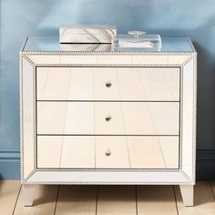 a mirrored chest of drawers in a room with blue walls and wooden floors, along with a white rug