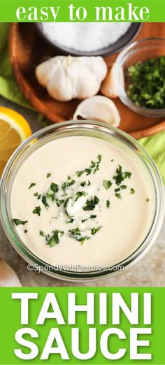 an easy to make tahini sauce in a glass bowl with herbs and lemons around it