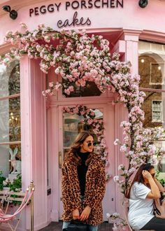 a woman standing in front of a pink building with flowers on the door and windows