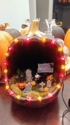 a pumpkin shaped pot with lights around it and decorations on the inside, sitting on a table in front of other pumpkins