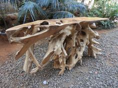 a wooden bench made out of driftwood sitting on top of a gravel ground next to trees