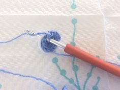 an orange crochet hook on top of a piece of white paper with blue thread