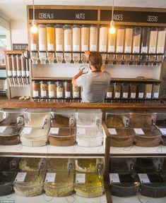 a woman standing behind a counter filled with lots of different types of spices and seasonings