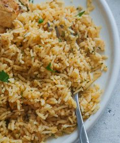 a white plate topped with rice and meat on top of a table next to a fork