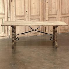 a wooden table with wrought iron legs in front of wood paneled walls and doors