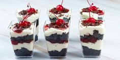 four desserts with cherries and whipped cream in glass cups on a wooden table