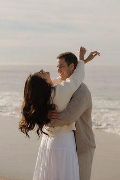 a man and woman hug on the beach while holding each other in front of the ocean