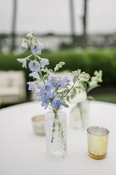 two vases filled with blue flowers sitting on top of a white table