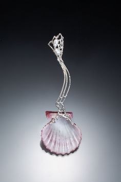 a pink sea shell with a silver chain hanging from it's side on a gray background