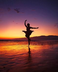 a woman is dancing on the beach at sunset