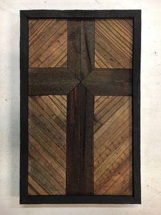 a cross made out of wood sitting on top of a white wall next to a black frame