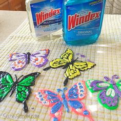 two bottles of windex are sitting on a table with butterfly magnets next to it