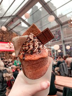 a person holding up a cupcake with chocolate on top