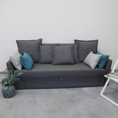 a grey couch with blue and gray pillows next to a green plant on a white chair