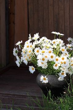 a vase filled with lots of white flowers on top of a wooden floor next to grass