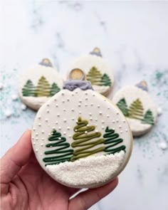 hand holding three decorated christmas cookies with trees on them and snow flakes in the background