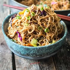 a bowl filled with noodles and vegetables next to chopsticks on a wooden table