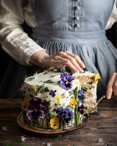 a woman in a blue dress holding a knife and cutting a cake with flowers on it