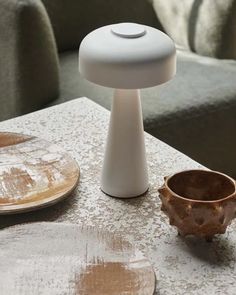 a small white table lamp sitting on top of a wooden table next to a brown bowl