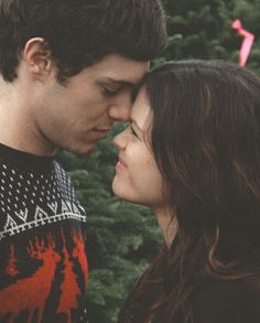 a young man and woman standing next to each other in front of some trees with pink streamers