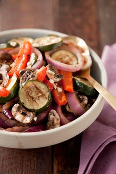 a white bowl filled with vegetables on top of a purple table cloth next to a wooden spoon