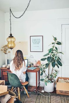 a woman sitting at a desk in front of a potted plant and boxes on the floor