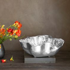 a metal bowl sitting on top of a table next to a vase filled with flowers