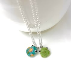 two necklaces are sitting on a white plate and one has a green turtle in the middle