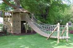 there is a tree house with a rope bridge in the yard and a play structure on the other side