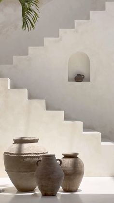 three vases sitting next to each other in front of a white wall and stairs