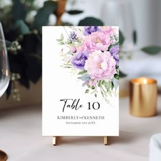 a table card with flowers on it sitting next to a wine glass and some candles