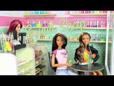 two barbie dolls sitting at a table in a store with the words sweet shop on it