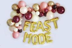 the words feast mode spelled with balloons in gold and burgundy colors on a white background