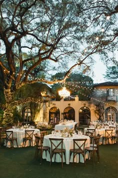 an outdoor dining area with white tablecloths and lights strung from the tree branches