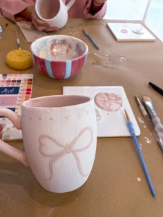 a person sitting at a table with some cups and paintbrushes in front of them