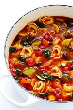 a pot filled with pasta and vegetables on top of a white table next to a spoon