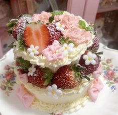 a three layer cake with strawberries and flowers on the top is sitting on a plate