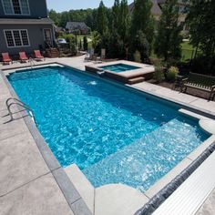 an empty swimming pool with lounge chairs around it and a fire pit in the back yard