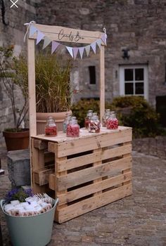 a wooden cart with jars and flowers on it next to a potted plant in front of a stone building